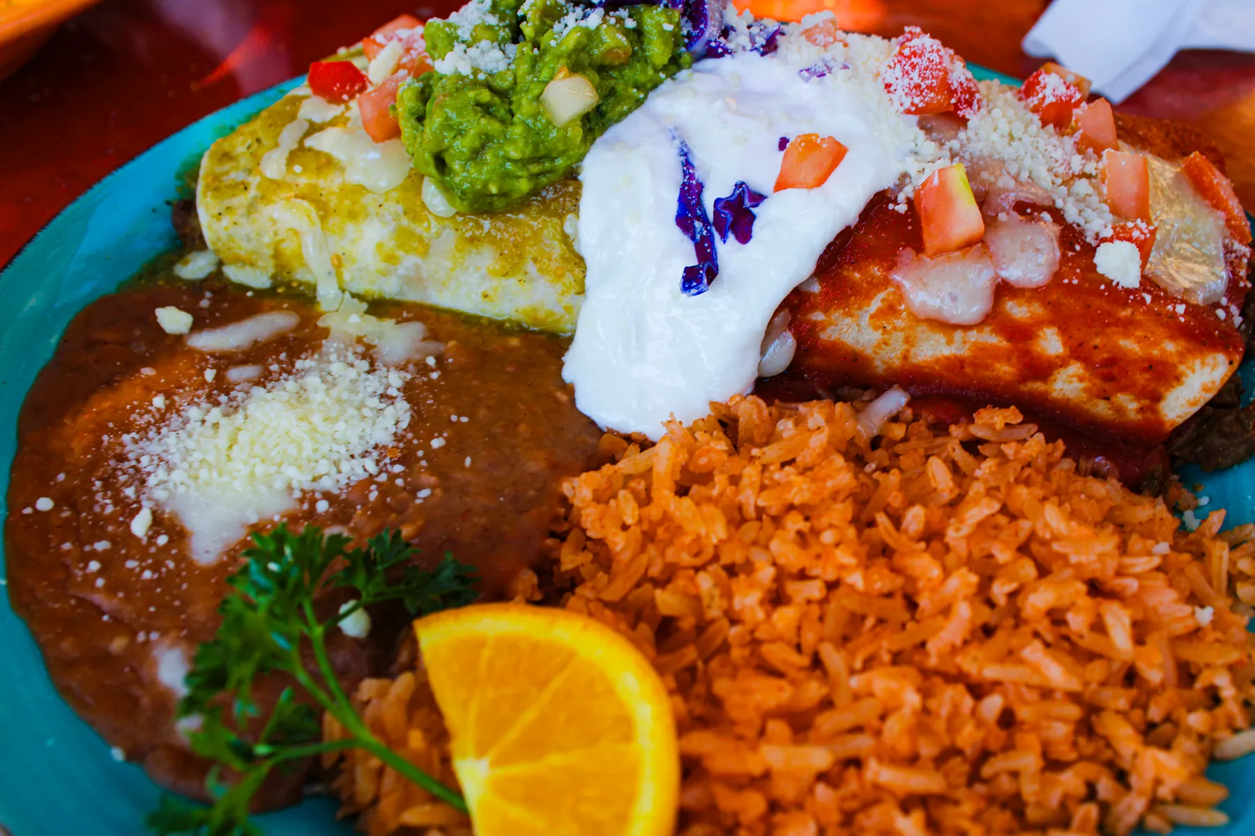 Two sauced entrées on one plate with rice, beans, guacamole and sour cream